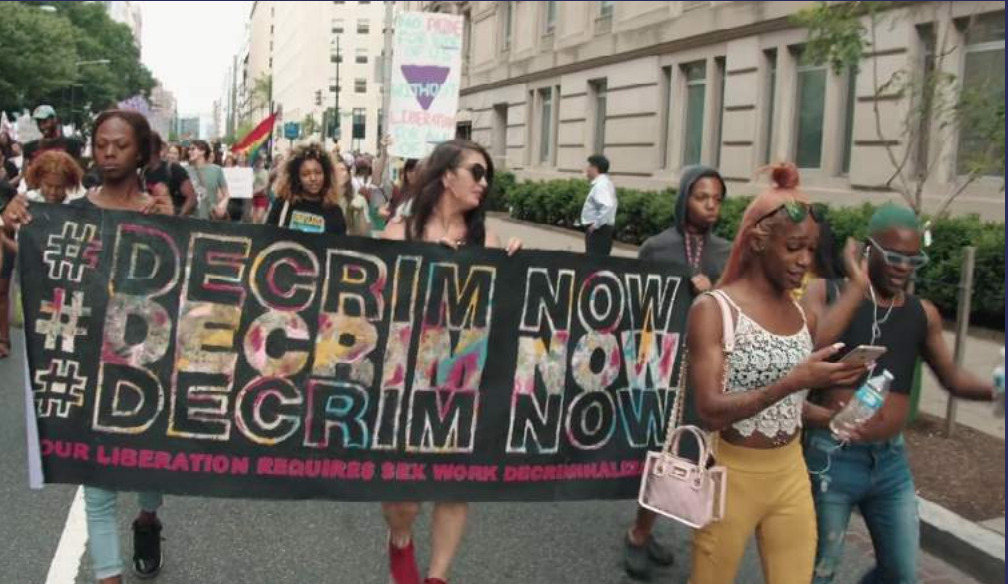 Photo of people marching and holding a #DecrimNow banner