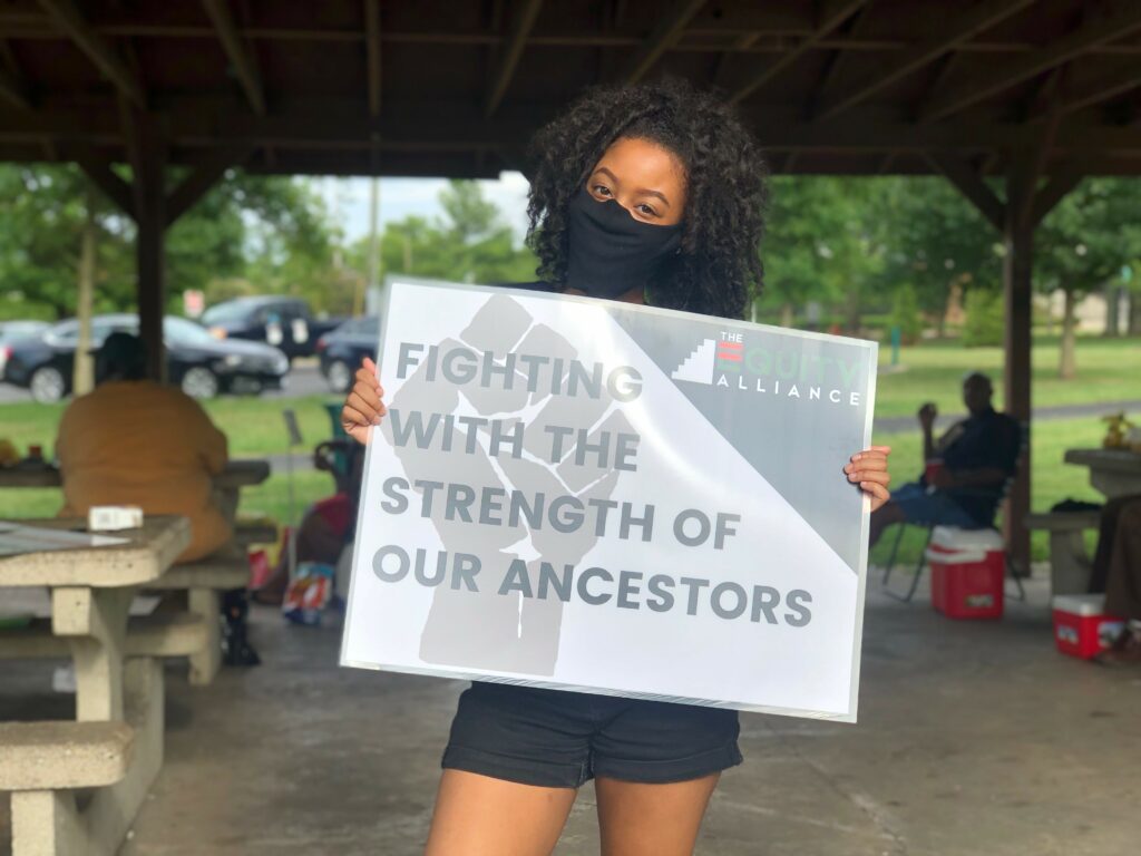 Person holding sign that says, 'fighting with the strength of our ancestors'