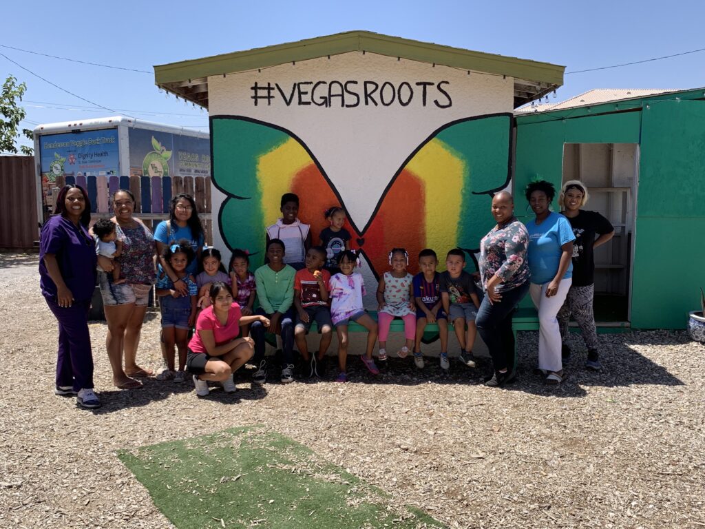 Organizers in front of a small building with a mural of a green, yellow, and orange butterfly, with the words #VegasRoots above the butterfly.